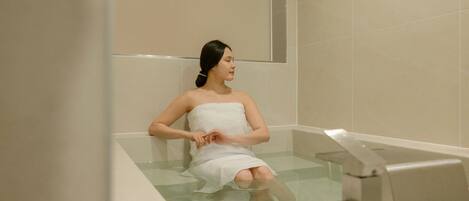A person sitting in a bathtub with a towel wrapped around their body.