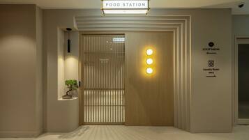 A hotel entrance with a food station sign, a wooden door with a vertical light strip, and a sign for a sauna and laundry room.