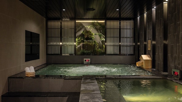Zona de baño termal con indicador de temperatura, estructura de madera y vistas a plantas de interior.
