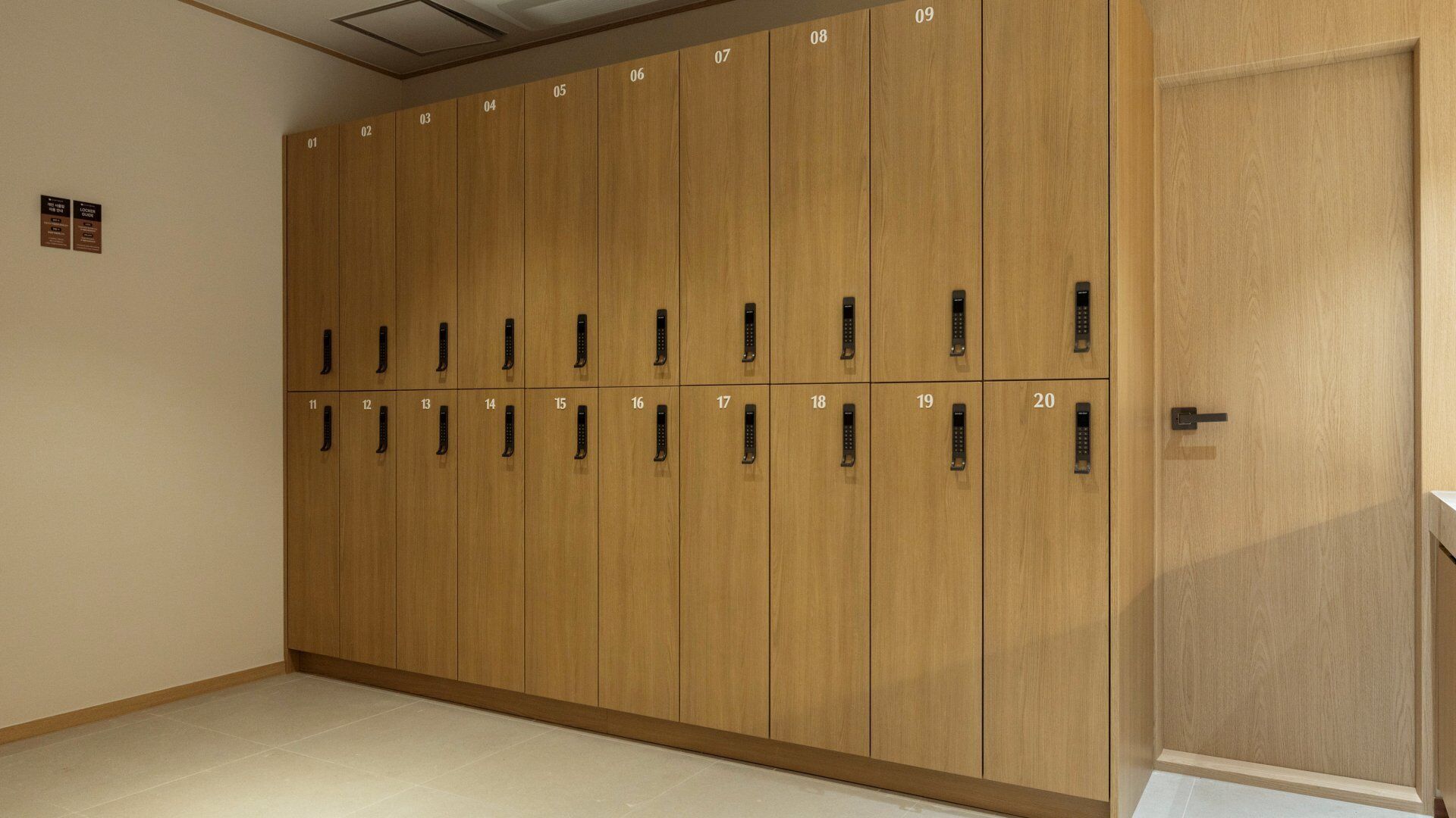 Una fila di armadietti in legno con ante numerate, un pavimento piastrellato e una porta sulla destra.