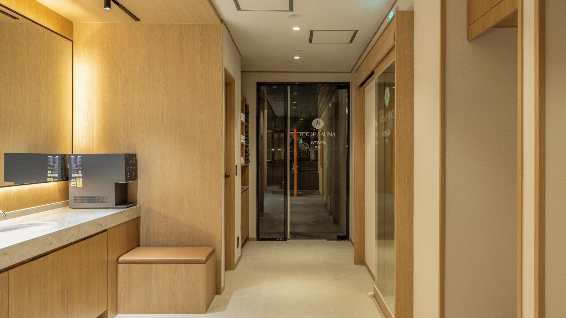 A modern bathroom with a wooden vanity, a digital shower control panel, and a glass door leading to a spa area.