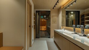 Un baño moderno con un espejo grande, un lavamanos y la entrada a una sauna.