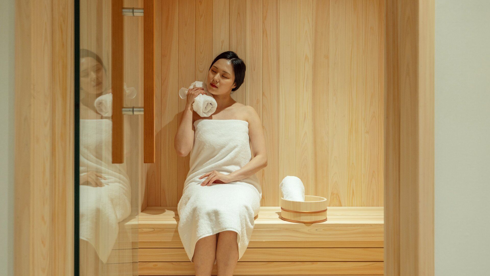 A person in a wooden sauna with a towel wrapped around them, sitting on a bench.