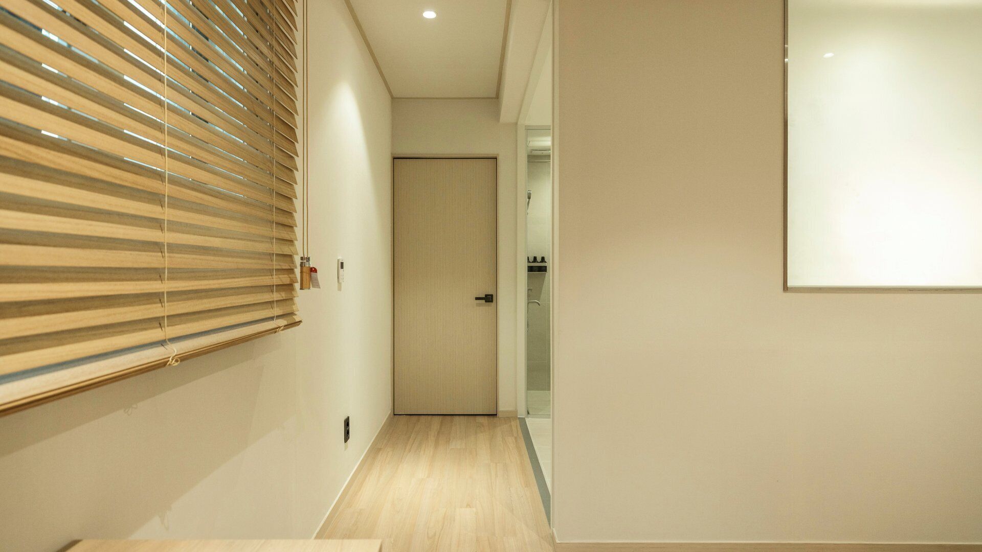 A hallway with wooden blinds, a door, and a view into a bathroom.