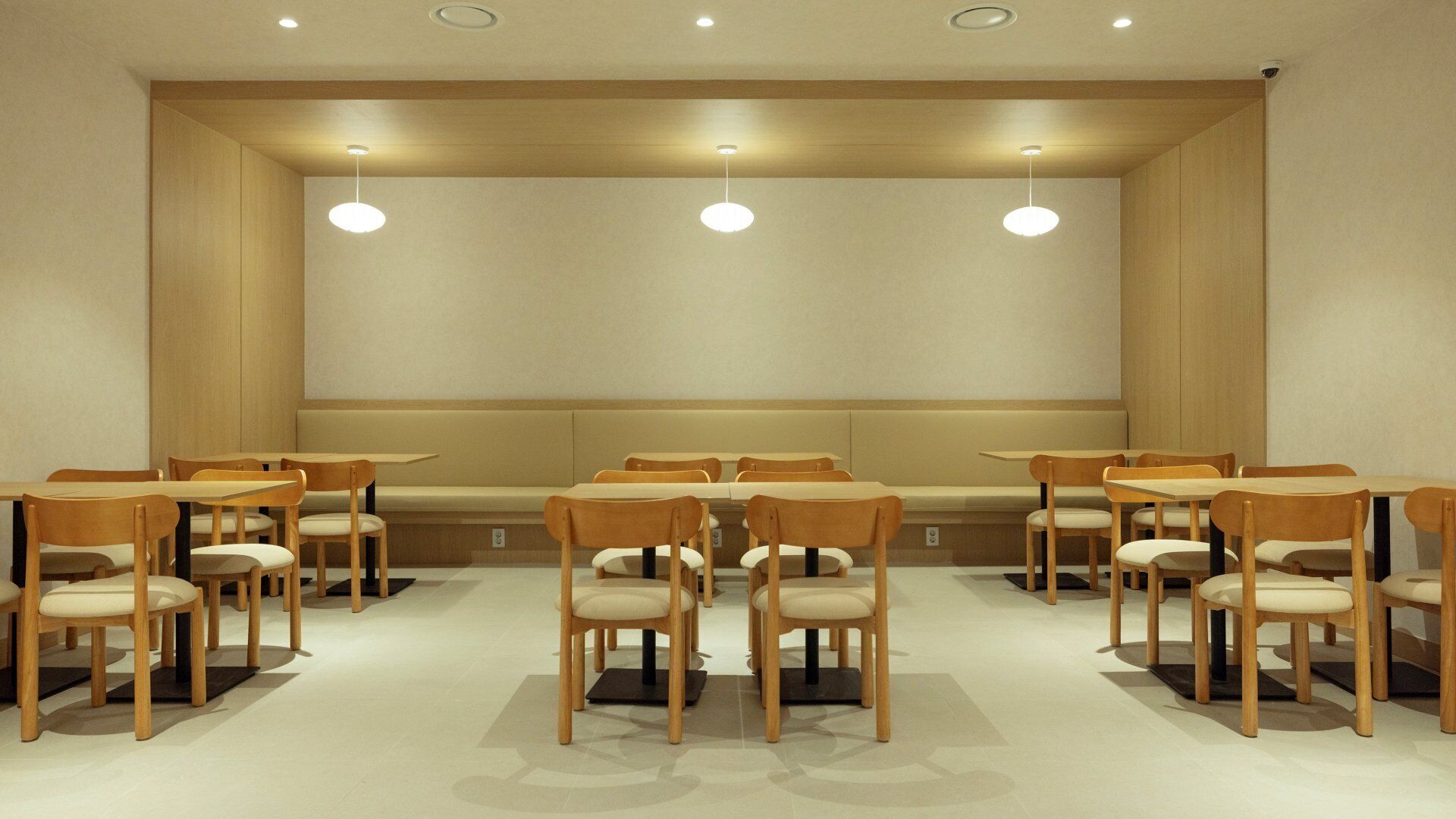 Uma sala de conferências com mesas e cadeiras de madeira, luminárias embutidas no teto e paredes em tom neutro.
