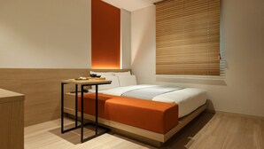 Una habitación de hotel moderna con cama, mesita de noche y ventana con persianas.