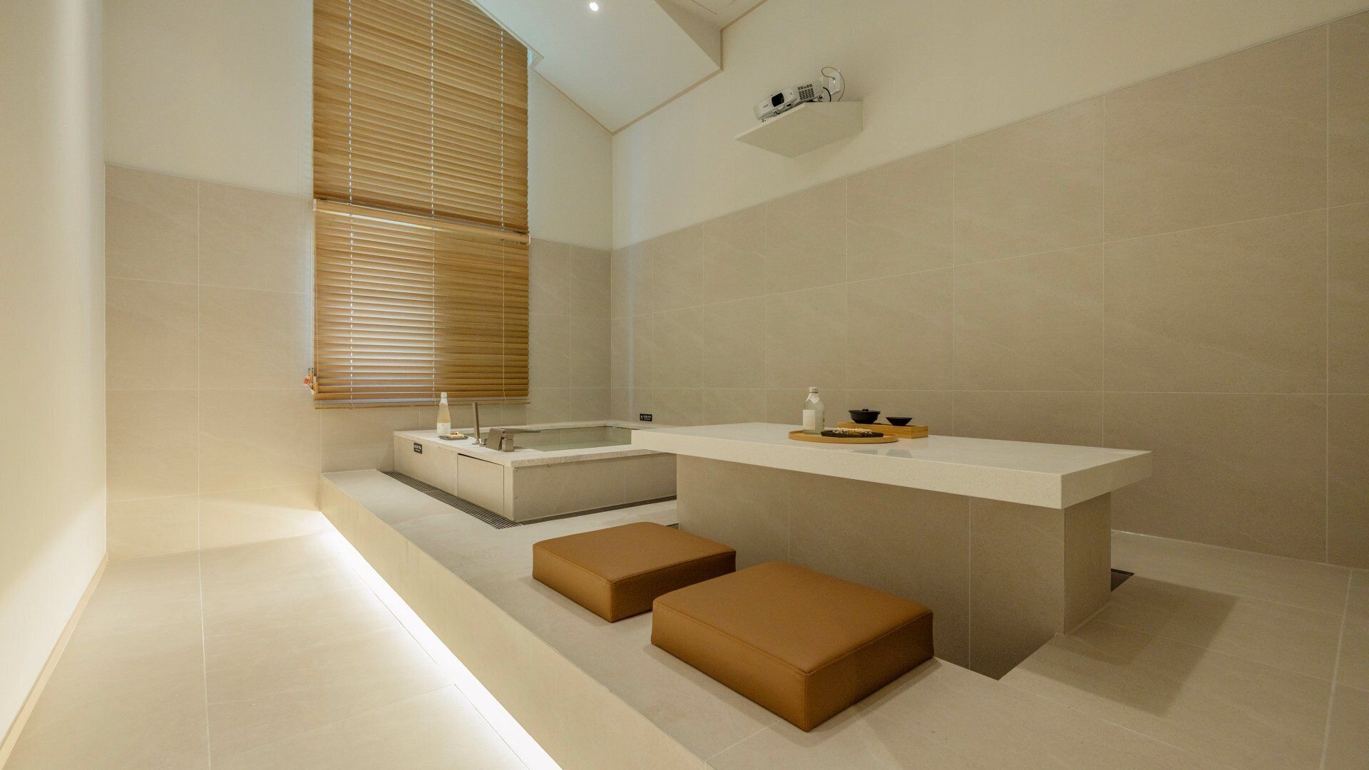 Un baño moderno con una bañera, un tocador con espejo y dos otomanas.
