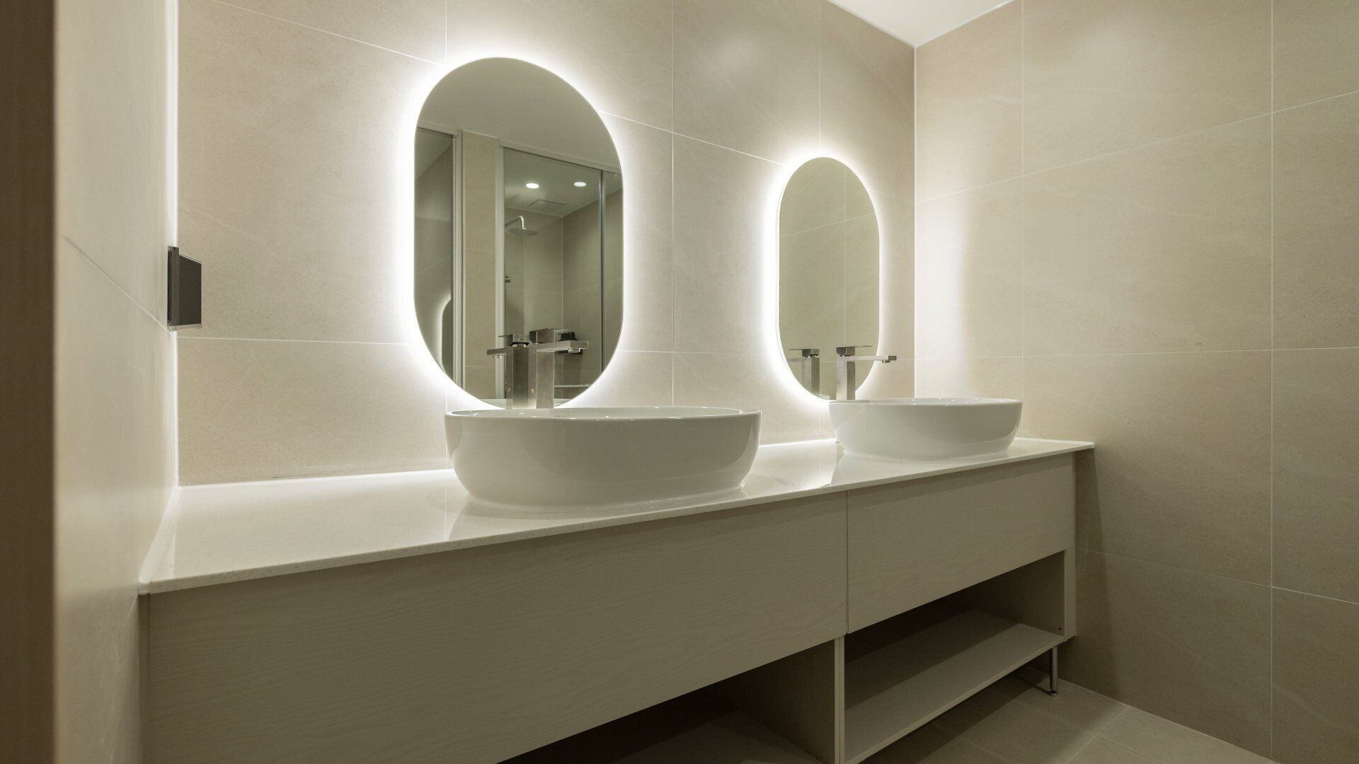 Een moderne badkamer met twee ovale spiegels, een wit wastafelmeubel en een strak design.