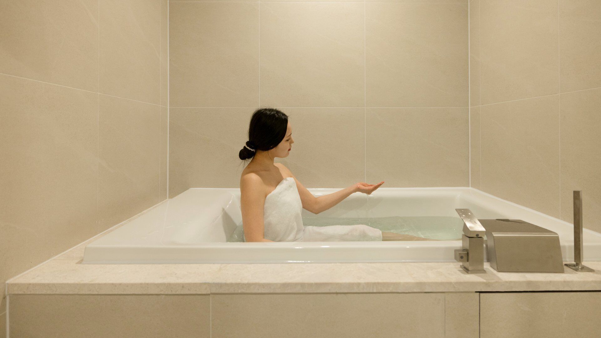 Una persona en una bañera con una toalla, un grifo y un panel de control.