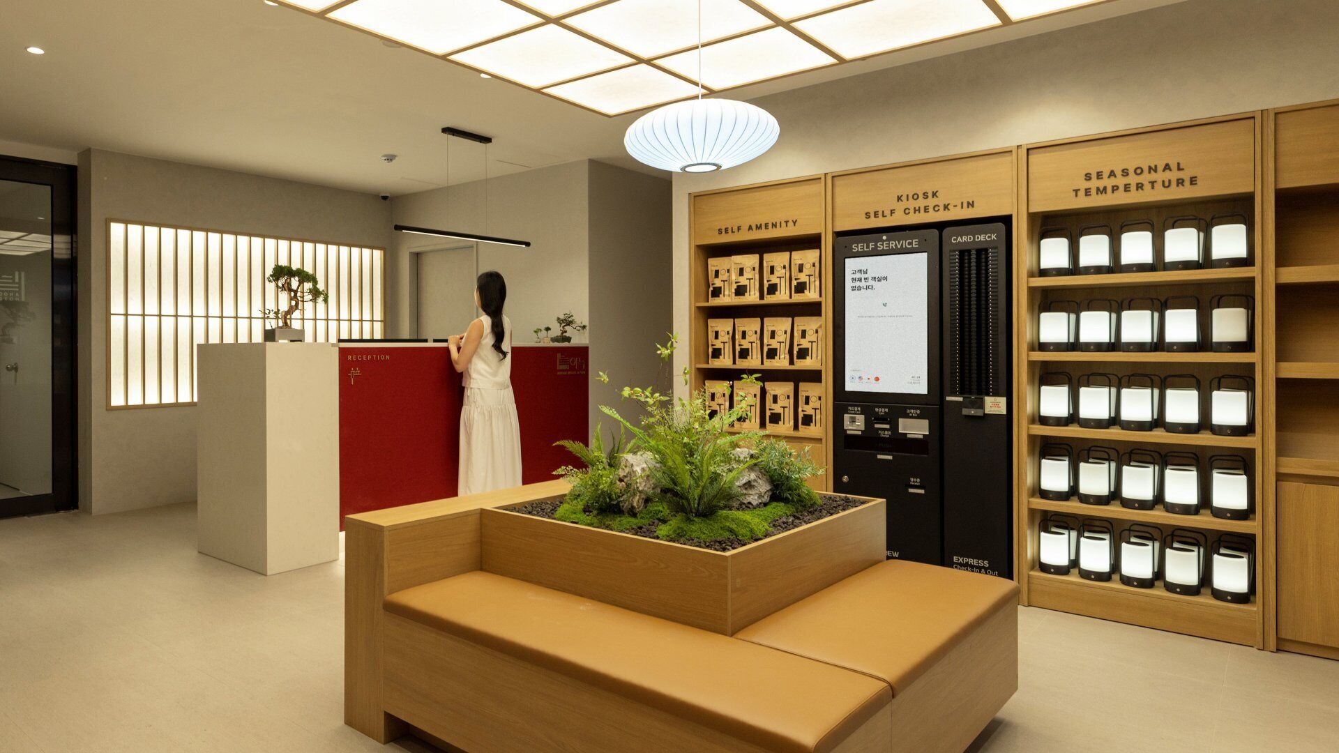 A reception area with a woman standing by the desk, a self-service kiosk, and a seasonal temperature display.
