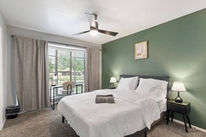 A bedroom with a bed, two bedside tables with lamps, a ceiling fan, a window with curtains, and a chair. - Arlington 2BR | AT&T, Globe Life, 6 Flags, Parking (Arlington)