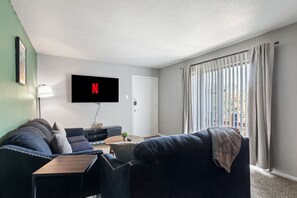 A living room with a sofa, a coffee table, a TV mounted on the wall, and a sliding glass door. - Arlington 2BR | AT&T, Globe Life, 6 Flags, Parking (Arlington)