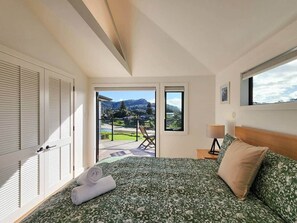 Ein Schlafzimmer mit Bett, Nachttisch, Lampe und Blick ins Freie.
