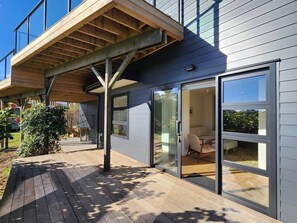 Ein modernes Haus mit einer Holzterrasse, Schiebetüren und einem überdachten Patio.