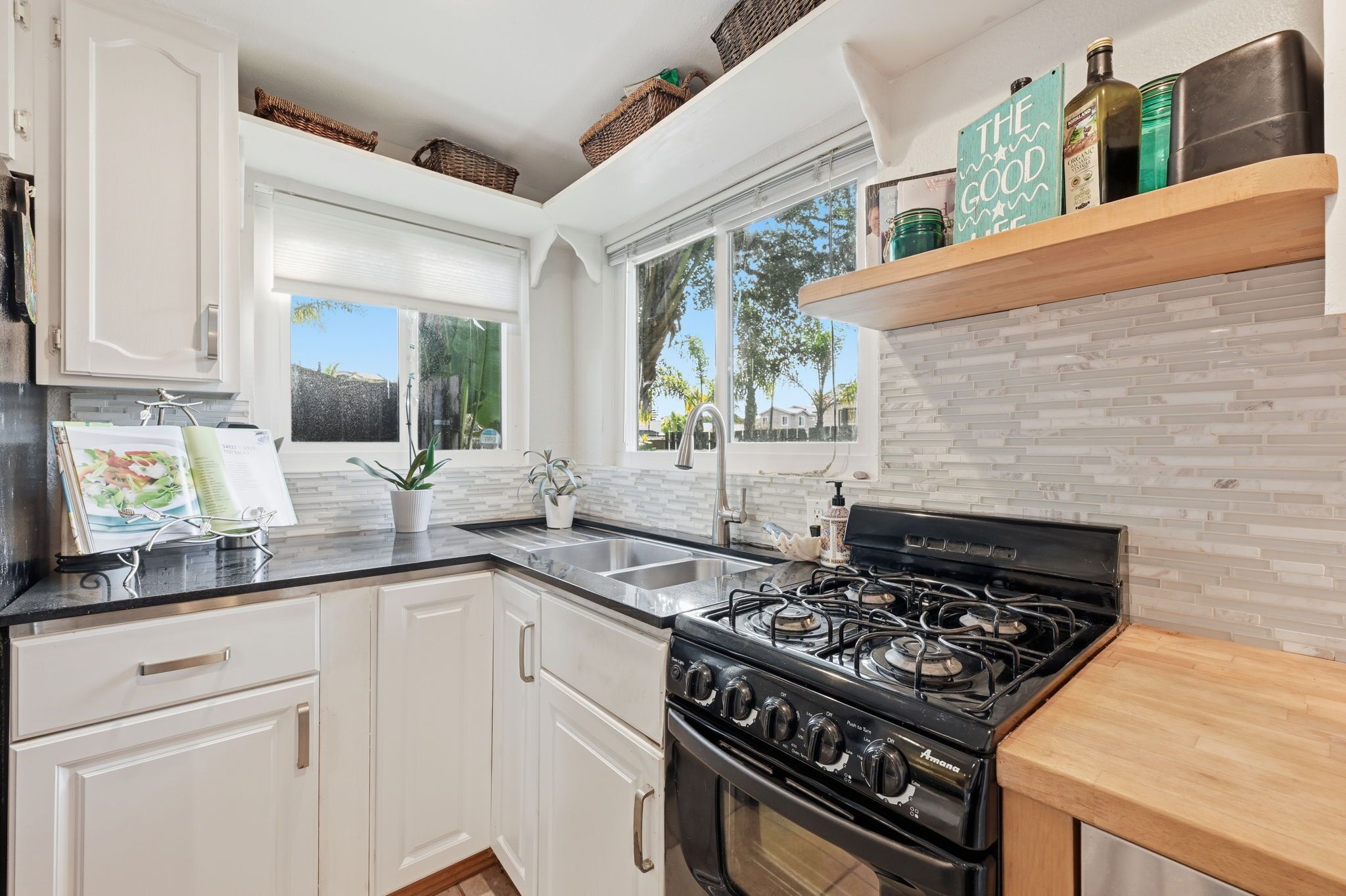 A kitchen with white cabinets, a black stove, and a window with a view of trees.