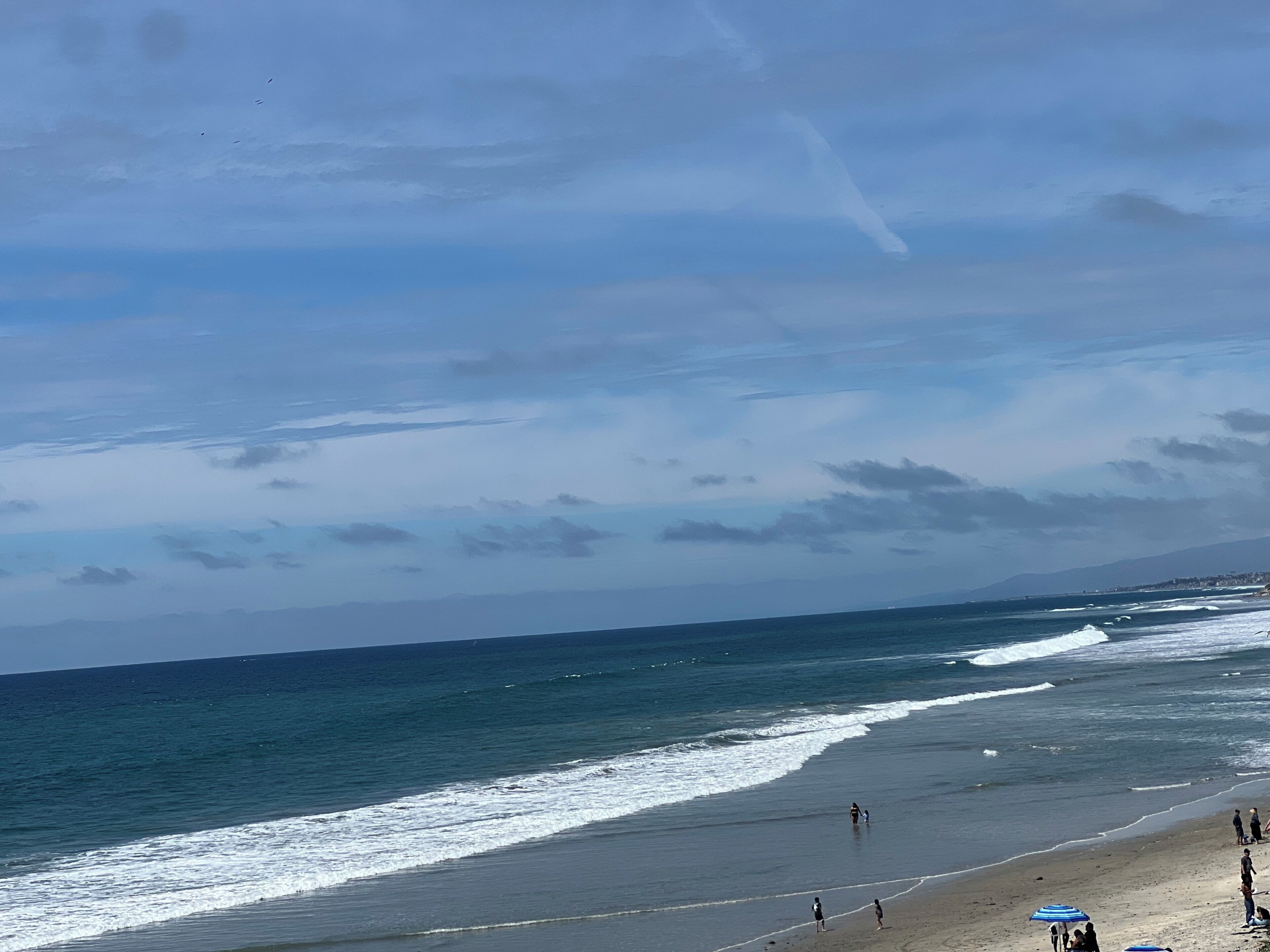 A beach with waves, people, and a clear sky.