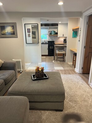 A living room with a grey sofa, a coffee table with a decorative centerpiece, and a kitchen in the background.
