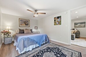 A bedroom with a bed, a nightstand, a lamp, a ceiling fan, and a large rug.