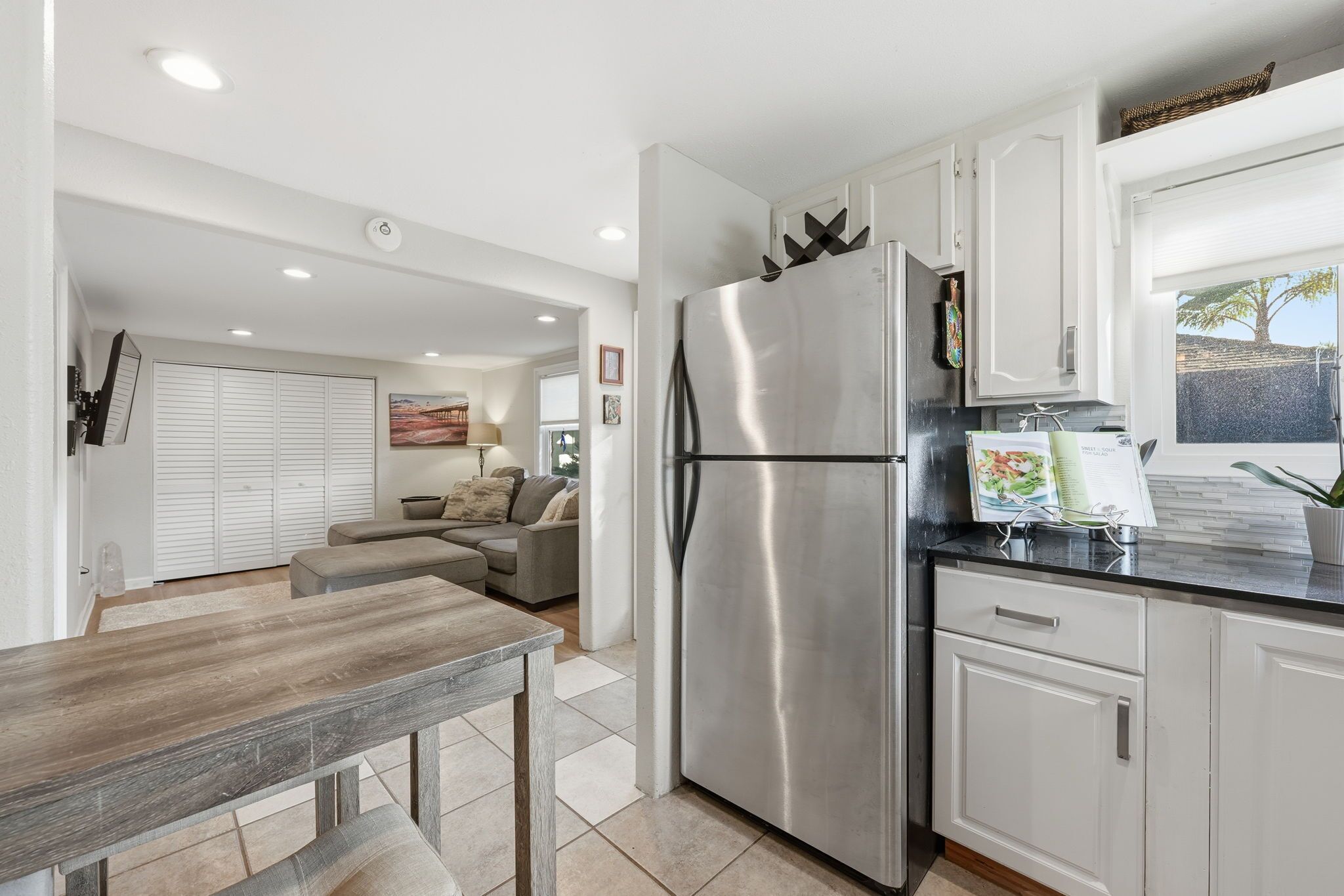 A modern kitchen with a stainless steel refrigerator, white cabinets, and a dining area with a wooden table.