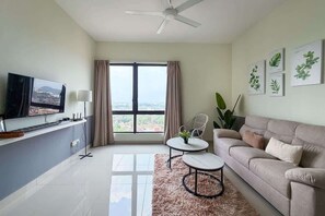 Un salon moderne avec un canapé, deux tables basses, un téléviseur et une grande fenêtre avec des rideaux.