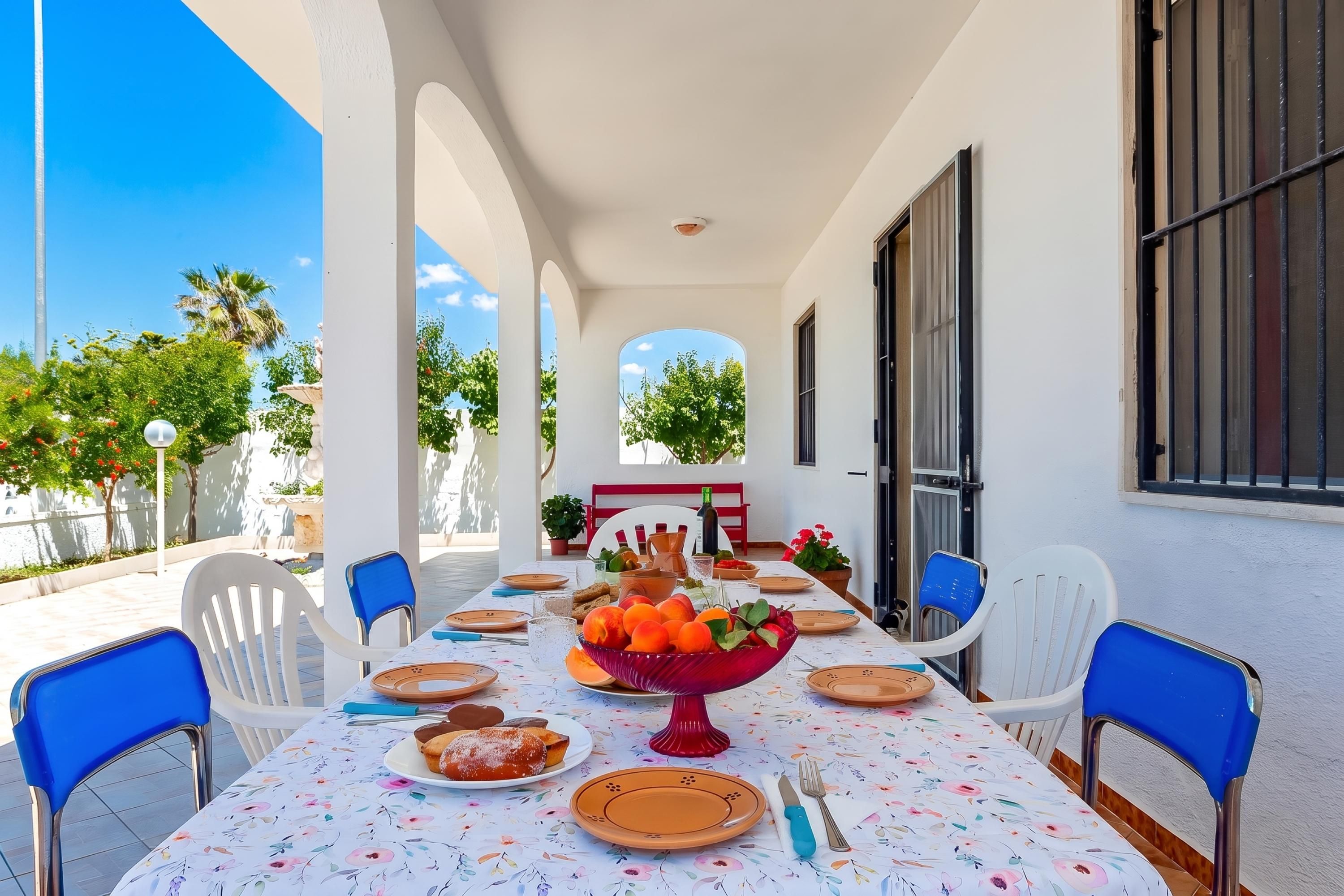 An outdoor dining area with a table set for a meal, surrounded by chairs, and a view of the sky and trees.