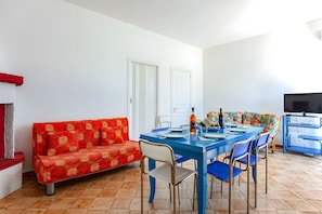 Ein Essbereich mit einem blauen Tisch, einem roten, gemusterten Sofa und einem Fernseher auf der rechten Seite.
