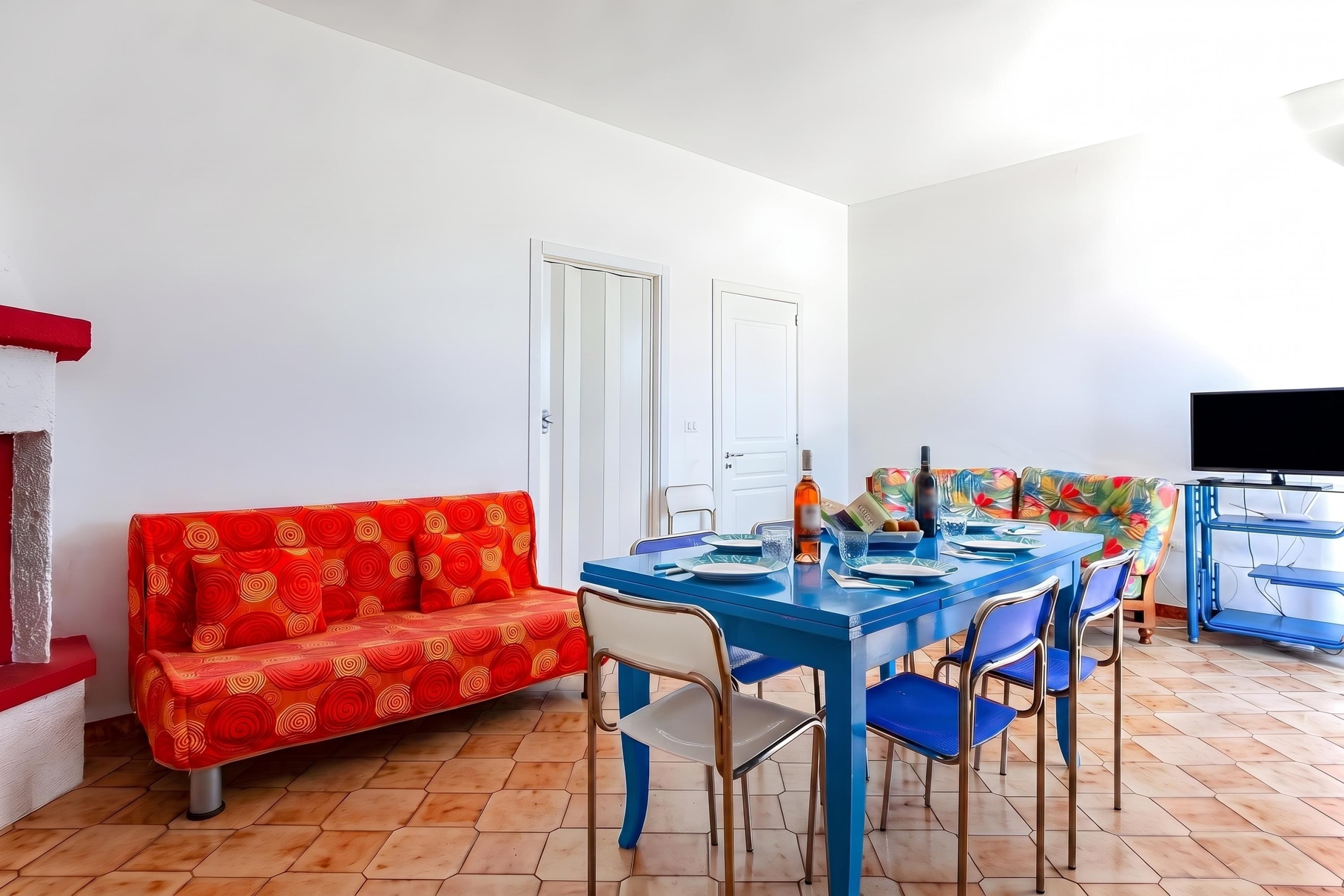 A dining area with a blue table, red patterned sofa, and a television on a stand.
