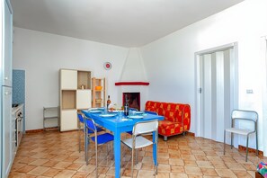 Un comedor con una mesa azul, sillas, un sofá rojo y blanco, y una zona de cocina con armarios y estufa.