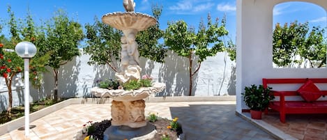A courtyard with a central fountain, a red bench, and potted plants.