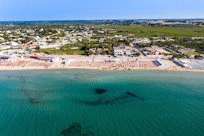 Vista aérea de uma cidade costeira com praia, edifícios e água azul cristalina.
