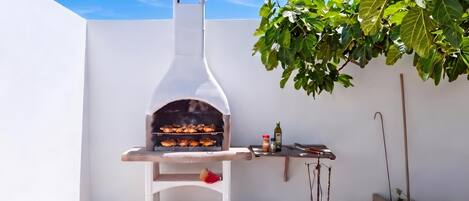 Un four à pizza d’extérieur blanc, doté d’une cheminée, une table avec une bouteille d’huile d’olive et un petit récipient d’épices.
