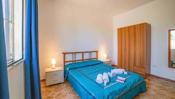 Quarto com cama, mesa de cabeceira, guarda-roupa e janela com cortinas.
