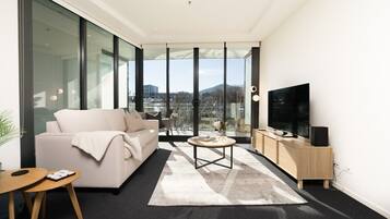 A modern living room with a sofa, coffee table, TV, and a view through large windows.
