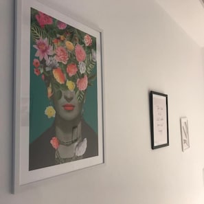 Une œuvre d’art encadrée est accrochée au mur, une autre œuvre, plus petite et également encadrée, se trouve à sa droite, et une troisième, encore plus petite, est placée en dessous.