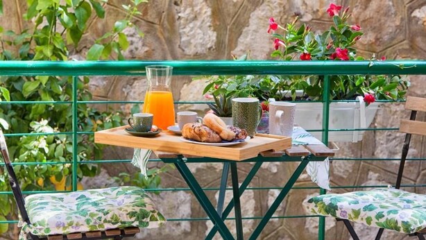 Un balcon avec une table préparée pour le petit-déjeuner, comprenant un verre de jus d’orange, des viennoiseries et une tasse.