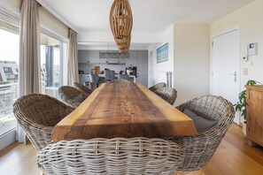 Ein Essbereich mit einem langen Holztisch, Korbstühlen und einer hängenden Leuchte.