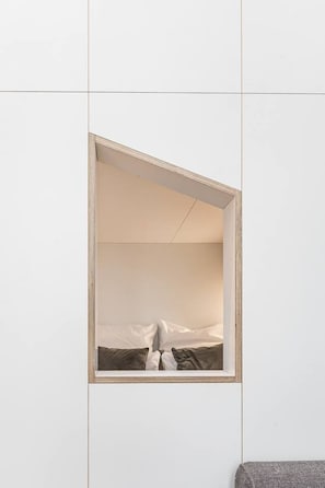 Ein schlichter Raum mit einem Bett, einem kleinen Fenster und einer schlichten Wand.