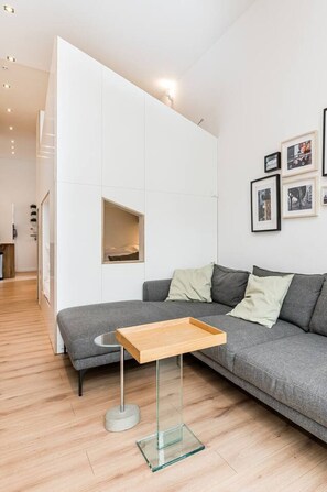 Ein modernes Wohnzimmer mit einem grauen Sofa, einem Glastisch und einer weißen Trennwand.