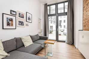 Un salon moderne avec un canapé gris, une petite table d’appoint et des tableaux encadrés accrochés au mur.