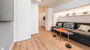 En moderne stue med en sofa, et sofabord og en vægmonteret hylde med indrammede billeder.