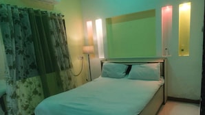 A hotel room with a bed, curtains, a lamp, and wall-mounted lights.