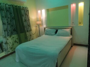 Una habitación de hotel con cama, cortinas, lámpara e iluminación en la pared.