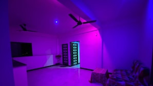 A room with a ceiling fan, a bed, a TV, and a door with a digital display.