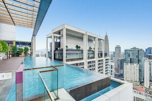 A rooftop infinity pool with a city view, a modern building with a glass facade, and a distinctive tower in the background. - The Platinum Suites by Soulasia (Kuala Lumpur)