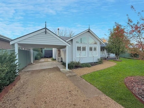 Eingeschossiges Haus mit überdachter Veranda, einem Vorgarten mit Rasen und Mulch sowie einem Baum mit Herbstlaub.