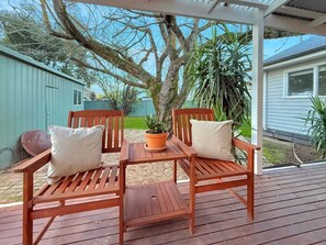 Eine Holzterrasse mit zwei Stühlen und einem Tisch, umgeben von Pflanzen und einem Haus.