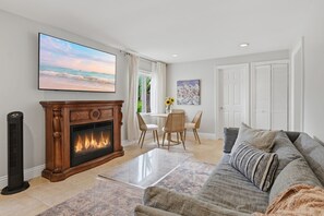 A living room with a fireplace, a sofa, a coffee table, and a TV displaying a beach scene.