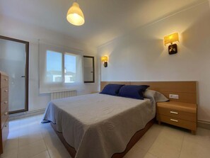 Ein Schlafzimmer mit einem Bett, Nachttischen, einer Kommode, einem Fenster und Wandleuchten.