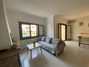 Ein Wohnzimmer mit einer Couch, einem kleinen Tisch, einem Fenster und einer Tür.