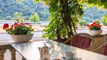 Ein Essbereich im Freien mit einem Tisch für zwei Personen, einer Karaffe, einer Tasse und einer Kuchenstück.